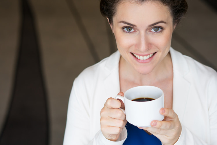 a woman is drinking a cup of coffee while smiling.
