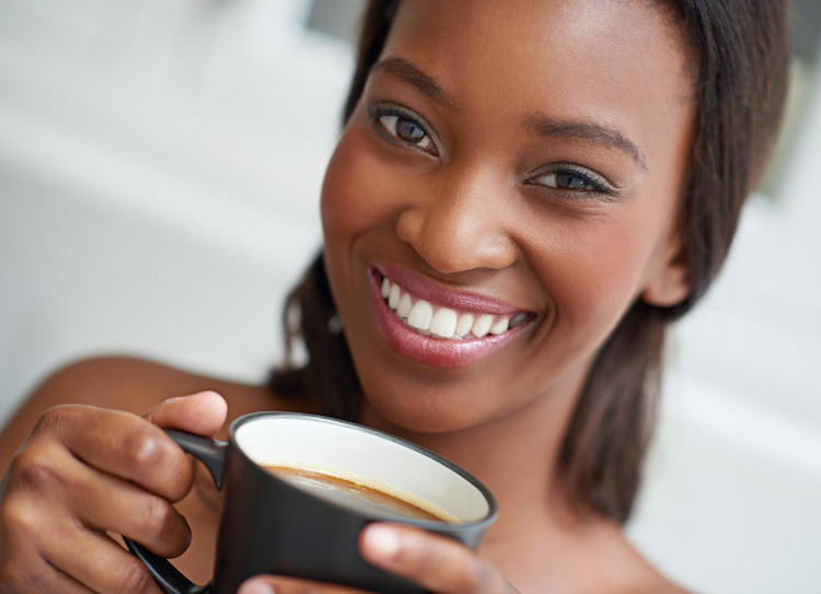 a woman holding a cup of coffee and smiling with her white teeth.