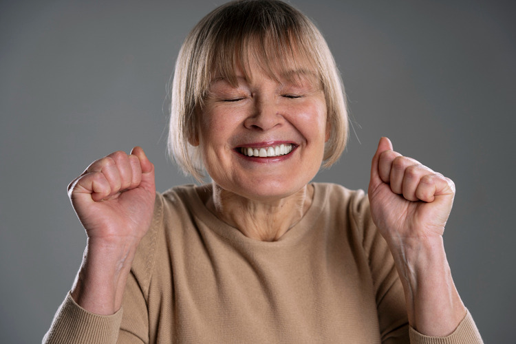 Happy senior woman showing straight teeth after Invisalign treatment, raising her hands in satisfaction