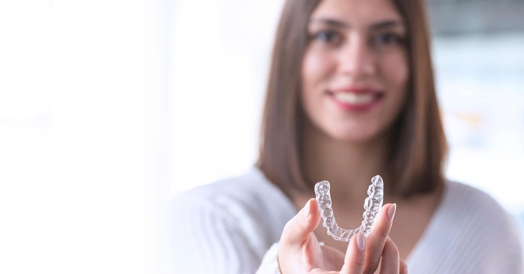 Woman holding an Invisalign clear aligner in her hands facing the camera