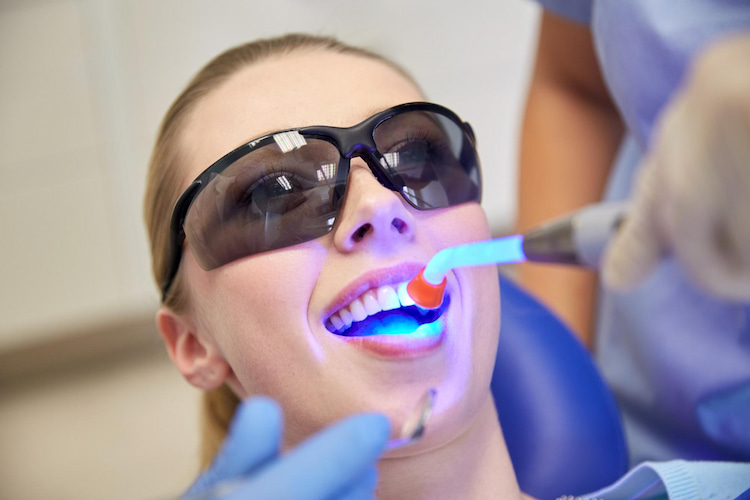 a woman is wearing protective glasses while getting her teeth whitened in a dental office. 