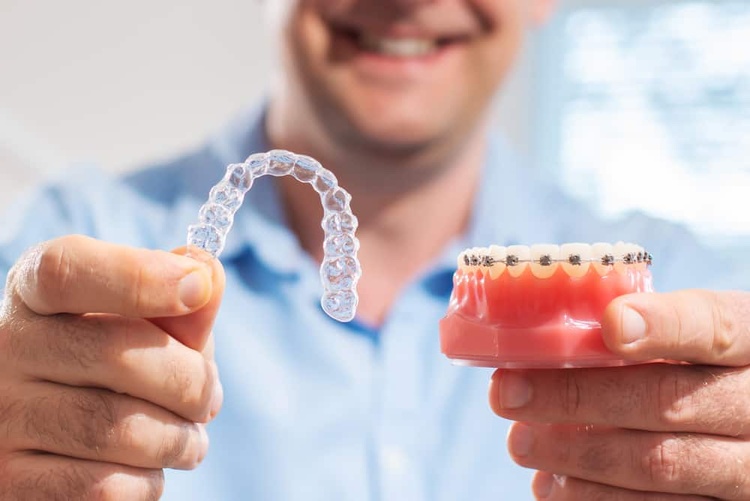 A man holding Invisalign aligners in one hand and traditional braces in the other, facing the camera for comparison.