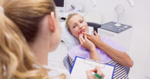 Young woman sitting in a dental chair with a concerned expression, holding her chin due to dental filling failure.