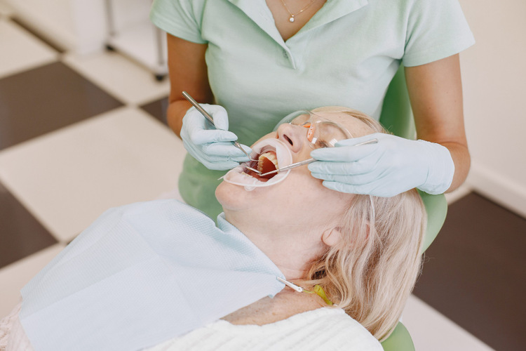 Woman lying in a dental clinic chair while a dentist performs restorative treatment on a failed dental filling.