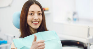 Young woman sitting in a dental chair, smiling happily while receiving CDCP dental coverage.