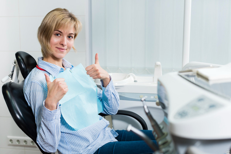 Young woman sitting in a dental chair, smiling happily after successfully renewing her CDCP coverage.
