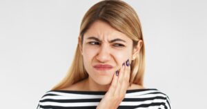 Young woman holding her jaw in pain due to a cracked tooth, unsure if it is a dental emergency.