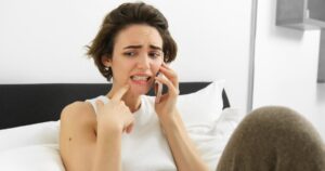 Woman sitting on her bed at home calling a same-day emergency dentist in Toronto for urgent tooth pain relief