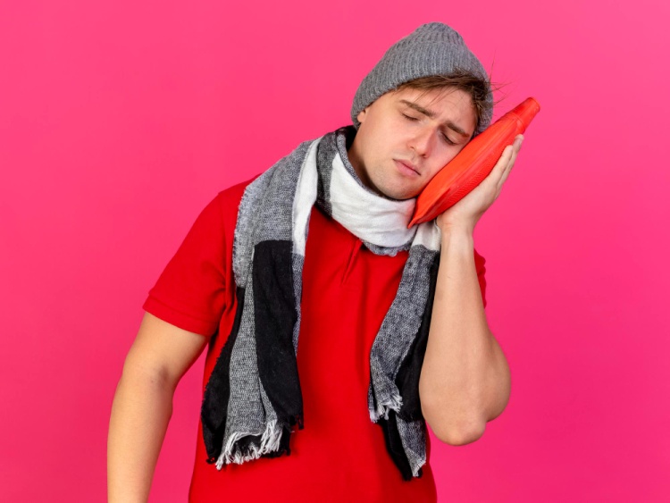 Young man applying a cold compress to his cheek to relieve severe tooth pain during a dental emergency