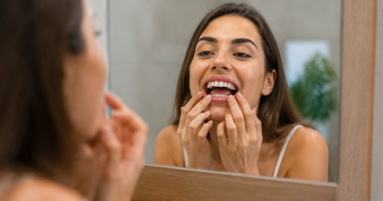 A young woman standing in front of a mirror, quickly evaluating whether she is a good candidate for porcelain veneers or not.