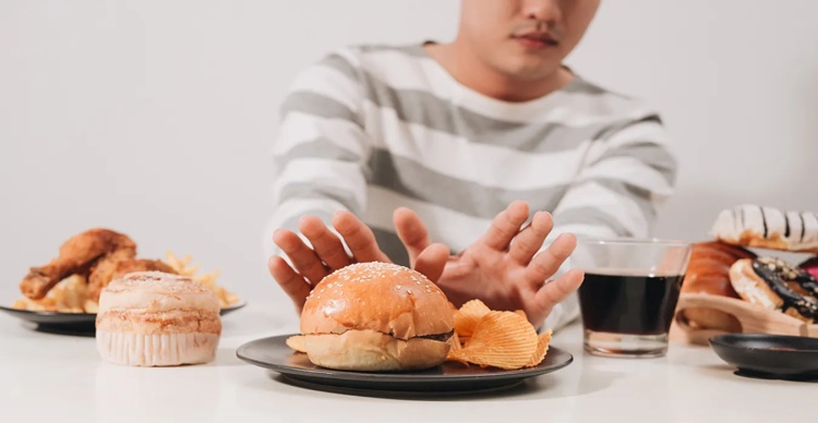 Man pushing away a plate of hard and greasy foods to avoid worsening a chipped tooth condition.