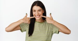 Healthy gums and teeth demonstration by a young woman pointing at her mouth to show oral health and gum condition.