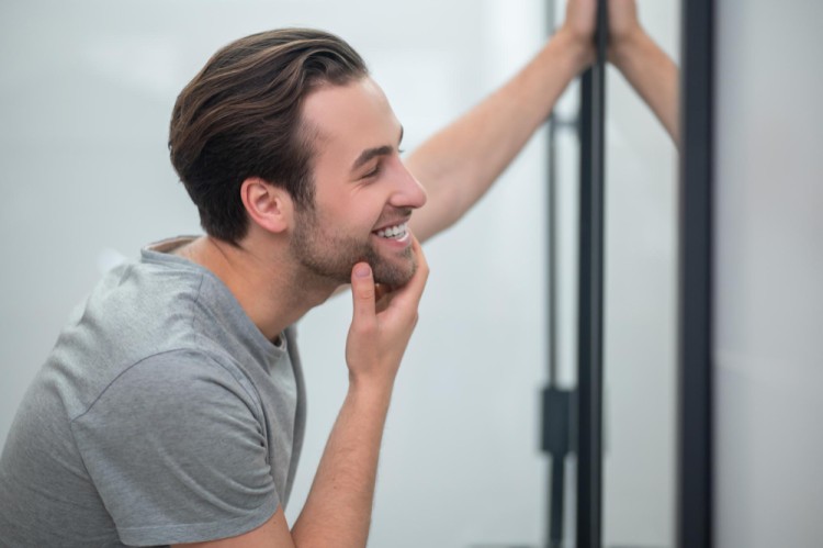 Young man smiling while checking his teeth and gum health in the mirror, reflecting good oral hygiene and dental care.