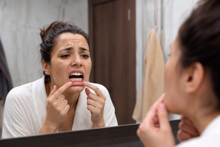 Woman looking worried while checking her gums in the mirror, concerned about possible gum disease or oral health issues.