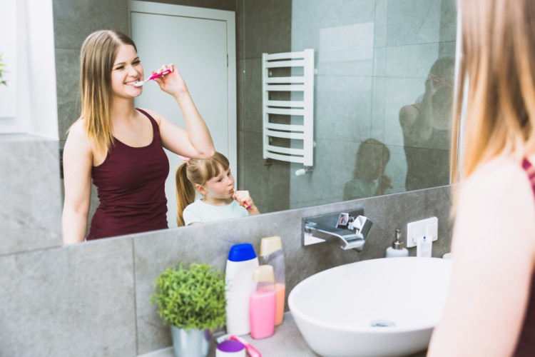 Mother and young daughter brushing their teeth together in front of a mirror, promoting healthy gums and good oral hygiene habits.