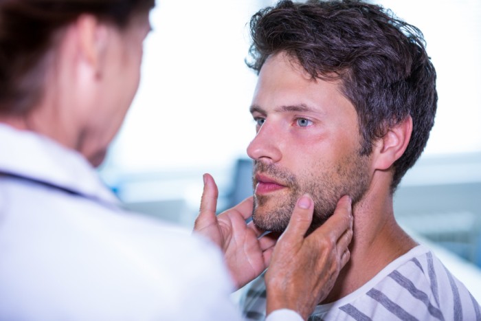 A dentist examining a male patient's jaw for TMJ disorder during a consultation.